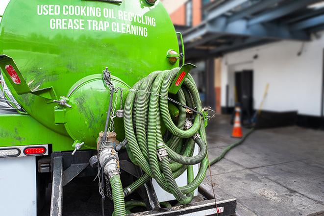 a professional plumber using a pump to empty a grease trap in Athens WI